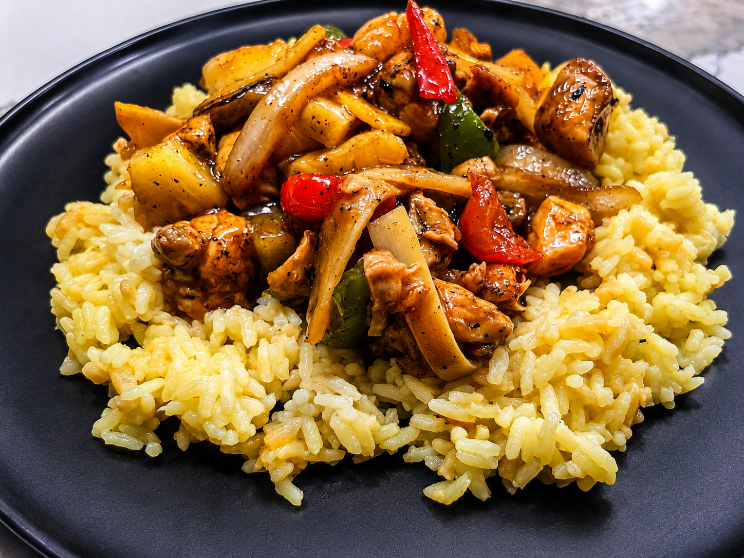 Chicken and pepper stir fry over yellow rice on a black plate