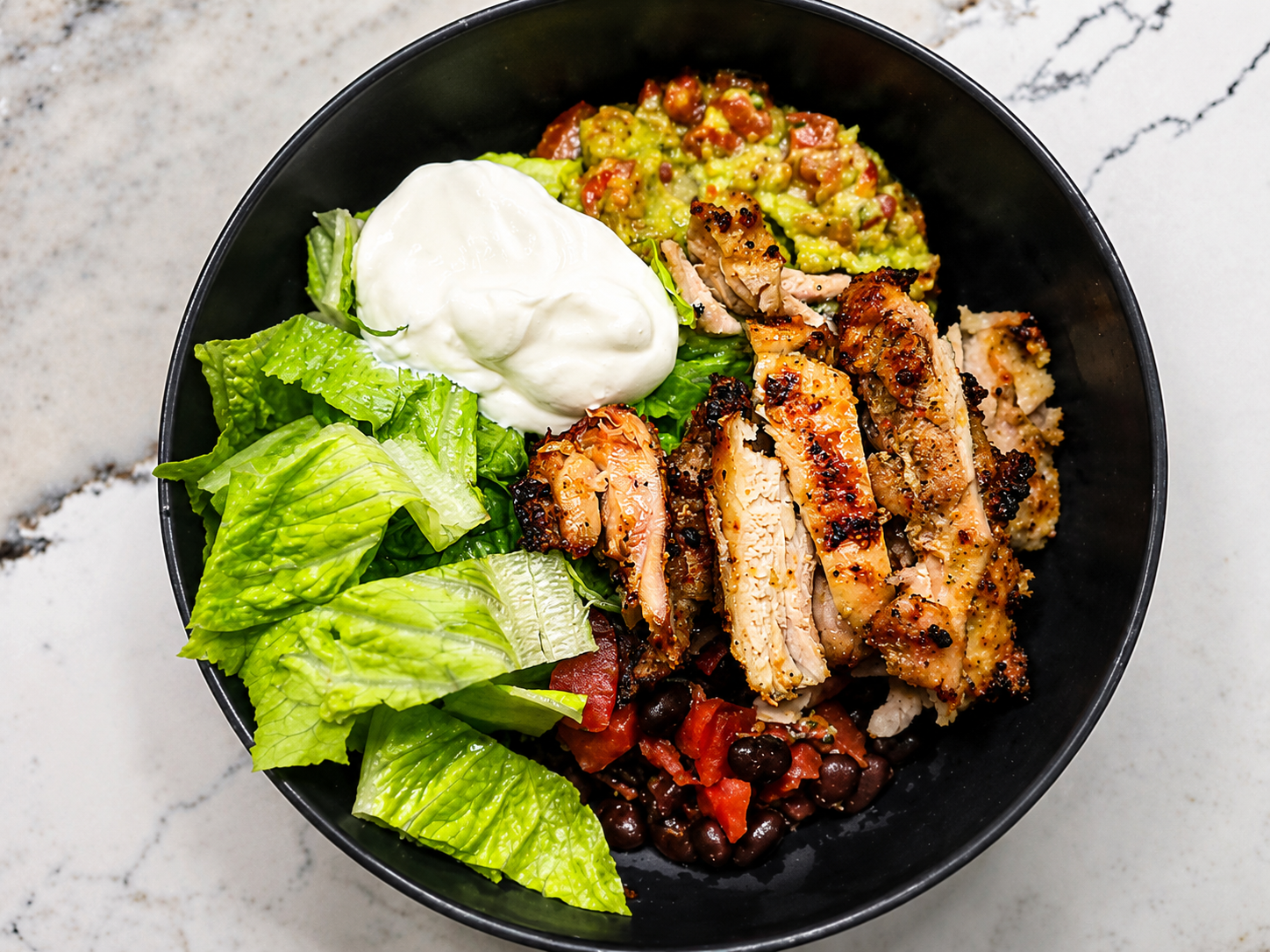 Grilled chicken bowl with romaine, guacamole, black beans, and sour cream