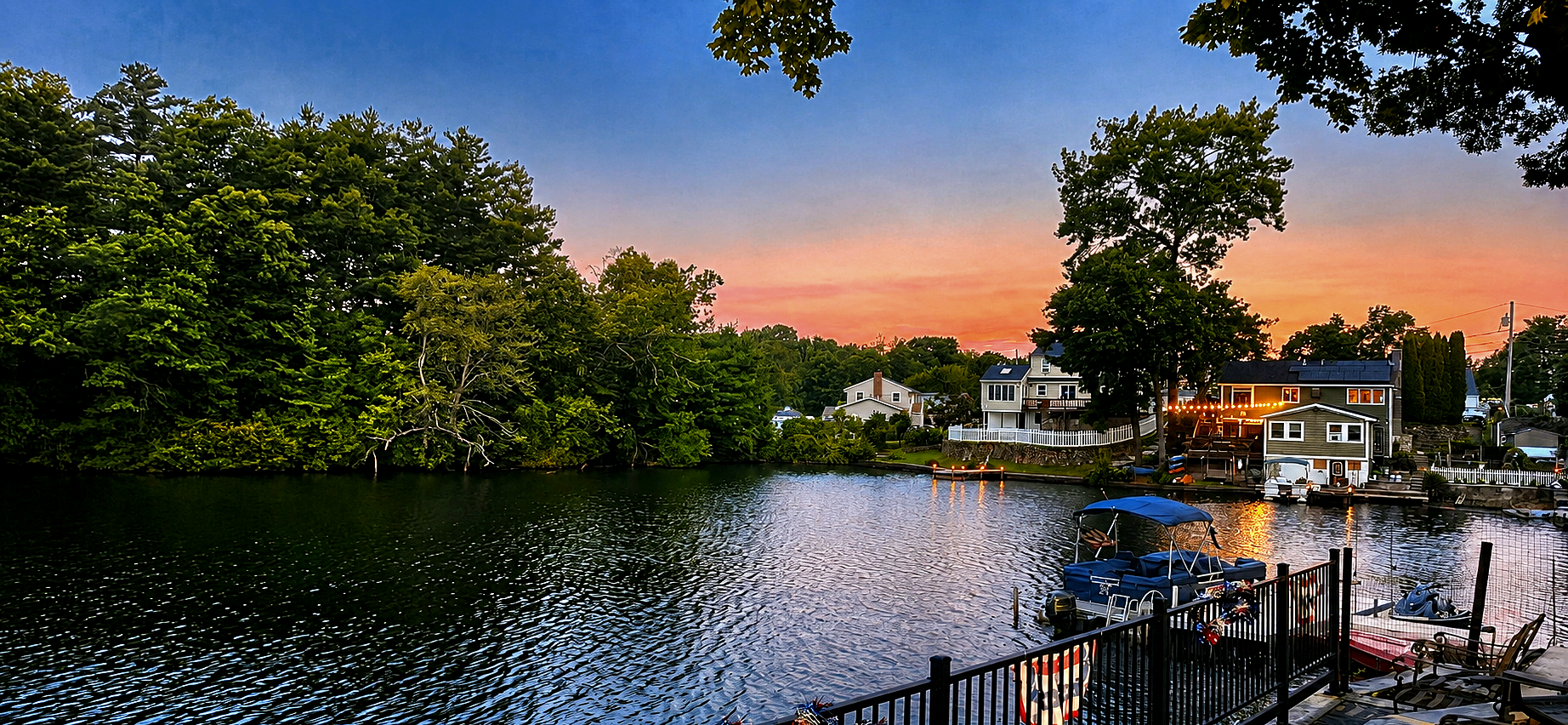 Lakeside homes and docked boats at sunset with orange sky reflected in the water